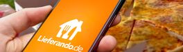 Logo des Lieferservices Lieferando.de wird auf einem Smartphone angezeigt, im Hintergrund eine gelieferte Pizza Von keBu.Medien
